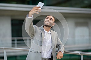 Joyful young businessman in suit taking a selfie outdoors