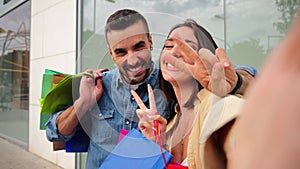 Joyful young caucasian real couple smiling and having fun taking a selfie portrait holding shopping bags at city store