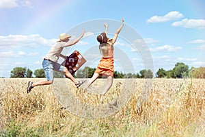 Joyful young couple having fun in wheat field. Excited man and woman running with retro leather suitcase on blue sky