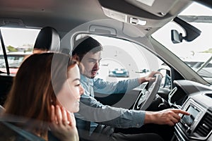 Joyful young couple sitting in a car dealership inside their new car