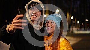 Joyful young couple taking selfie grimacing gesturing standing on winter street outdoors. Positive cheerful Asian man