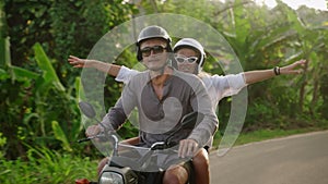 Joyful young couple traveling by motorbike. Two cheerful lovers ride motorcycle on jungle road. Girlfriend laugh