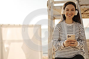 Joyful young fair-skinned girl in headphones holds phone on photo with place for text.