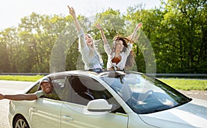 Joyful young friends having fun in their car, partying during road trip, traveling in countryside on summer vacation