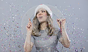 Joyful young girl with confetti. A beautiful blonde woman in a gray sweater and a Santa hat celebrates the New Year and Christmas