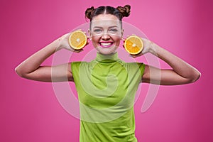 Joyful young girl with pink lips holding two sliced oranges