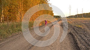 Joyful young girl running and jumping by country road near field. Autumn golden evening. Young Girl.