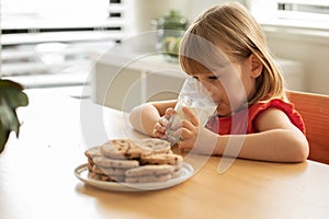 Joyful young girl savoring a glass of milk with a plate of cookies, perfect for a cozy snack time.