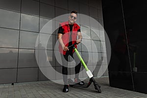 Joyful young hipster man in stylish red-black jeans clothes in sports sneakers in sunglasses with a vintage scooter stands