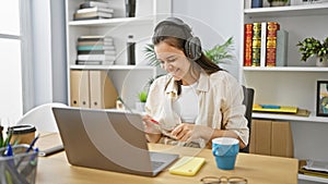 Joyful young hispanic woman worker having fun, dancing to music while working on her laptop at the office, exuding confidence