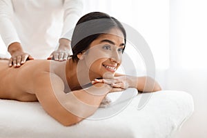 Joyful young indian woman getting body massage at spa