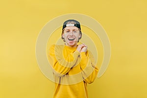 Joyful young man in a cap stands on a yellow background, looks at the camera and laughs