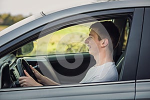 Joyful young man driving safe his new car, looking ahead at the street traffic. Contented teenage driver enjoying the ride, keeps