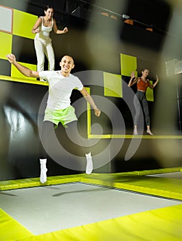 Joyful young man jumping on trampolines in colorful amusement park