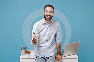 Joyful young man in shirt work near white desk with pc laptop isolated on blue background. Achievement business career