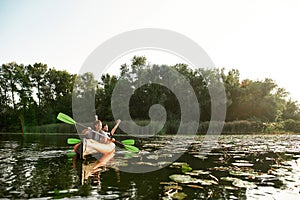 Joyful young mixed couple spending time together, kayaking on river surrounded by wild nature