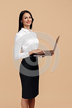 Joyful young modern business woman over beige background, working on laptop computer.