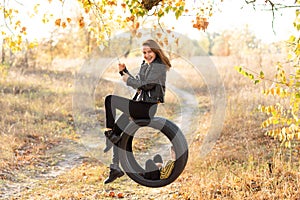 Joyful young mother having fun with her little son in nature, sitting together on a swing wheel