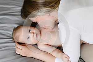 Joyful young mother plays with her baby lying on the bed, smiles, kisses the cheek, enjoys motherhood.Family, love,care.