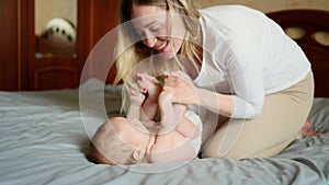 Joyful young mother plays with her baby lying on the bed,smiles,kisses,enjoys motherhood.Concept of family,love and care