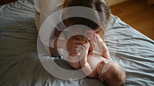 Joyful young mother plays with her baby lying on the bed,smiles,kisses,enjoys motherhood.Concept of family,love and care