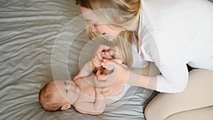 Joyful young mother plays with her baby lying on the bed,smiles,kisses,enjoys motherhood.Concept of family,love and care