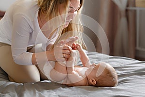Joyful young mother plays with her baby lying on the bed,smiles,kisses,enjoys motherhood.Concept of family,love and care