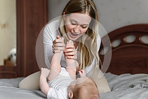 Joyful young mother plays with her baby lying on the bed,smiles,kisses,enjoys motherhood.Concept of family,love and care