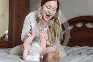 Joyful young mother plays with her baby lying on the bed,smiles,kisses,enjoys motherhood.Concept of family,love and care