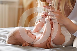 Joyful young mother plays with her baby lying on the bed,smiles,kisses,enjoys motherhood.Concept of family,love and care