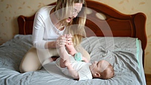 Joyful young mother plays with her child lying on the bed,smiles,kisses feet,enjoys motherhood. Family,love,care concept