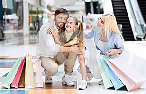 Joyful Young Parents Hugging Little Daughter Sitting In Mall Store