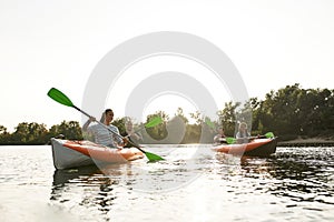 Joyful young people kayaking together on a river, spending weekend outdoors on a summer day