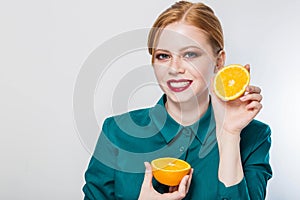 Joyful young redhead woman holding juicy oranges before her eyes. Healthy eating concept.