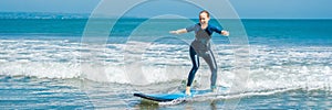 Joyful young woman beginner surfer with blue surf has fun on small sea waves. Active family lifestyle, people outdoor