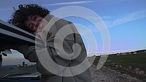 Joyful Young Woman Enjoying Freedom on a Countryside Drive, Leaning out of Car Window at Dusk, with Expansive Blue Sky