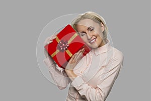 Joyful young woman holding gift box on gray background.