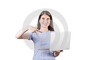 Joyful young woman holding a laptop in her hand and pointing at it with forefinger as recommendation, isolated on white background