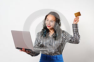 A joyful young woman holding a plastic Bank card and a laptop. Studio photo on white background