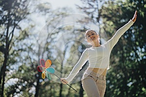 Joyful young woman playing with a colorful pinwheel in a sunny park