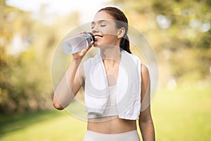 A joyful young woman quenches her thirst by drinking water from a clear bottle