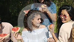 Joyful young woman talking to friends dancing and eating watermelon on picnic outdoors