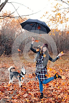 Joyful young woman throwing leaves and playing with her dog in the autumn park