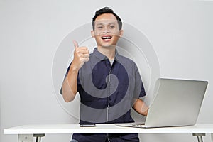 joyfull happy asian man on video call online meeting giving thumb up sign at workplace while sitting in front of laptop computer.