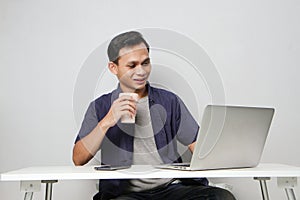 joyfull happy asian man at workplace while sitting in front of laptop computer. on isolated background