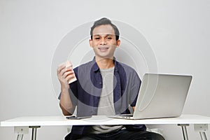 joyfull happy asian man at workplace while sitting in front of laptop computer. on isolated background