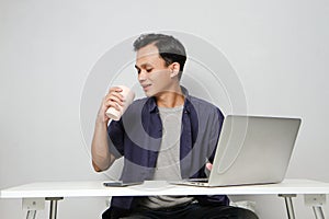 joyfull happy asian man at workplace while sitting in front of laptop computer. on isolated background