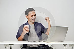 joyfull happy asian man at workplace while sitting in front of laptop computer. on isolated background