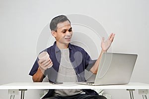 joyfull happy asian man at workplace while sitting in front of laptop computer. on isolated background