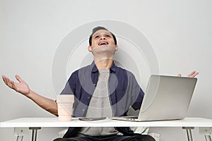 joyfull happy asian man at workplace while sitting in front of laptop computer. on isolated background